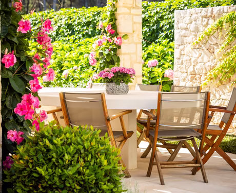 Einblick Strandbar mit Holzstühlen, überdachter Pergola und pinken Blumen
