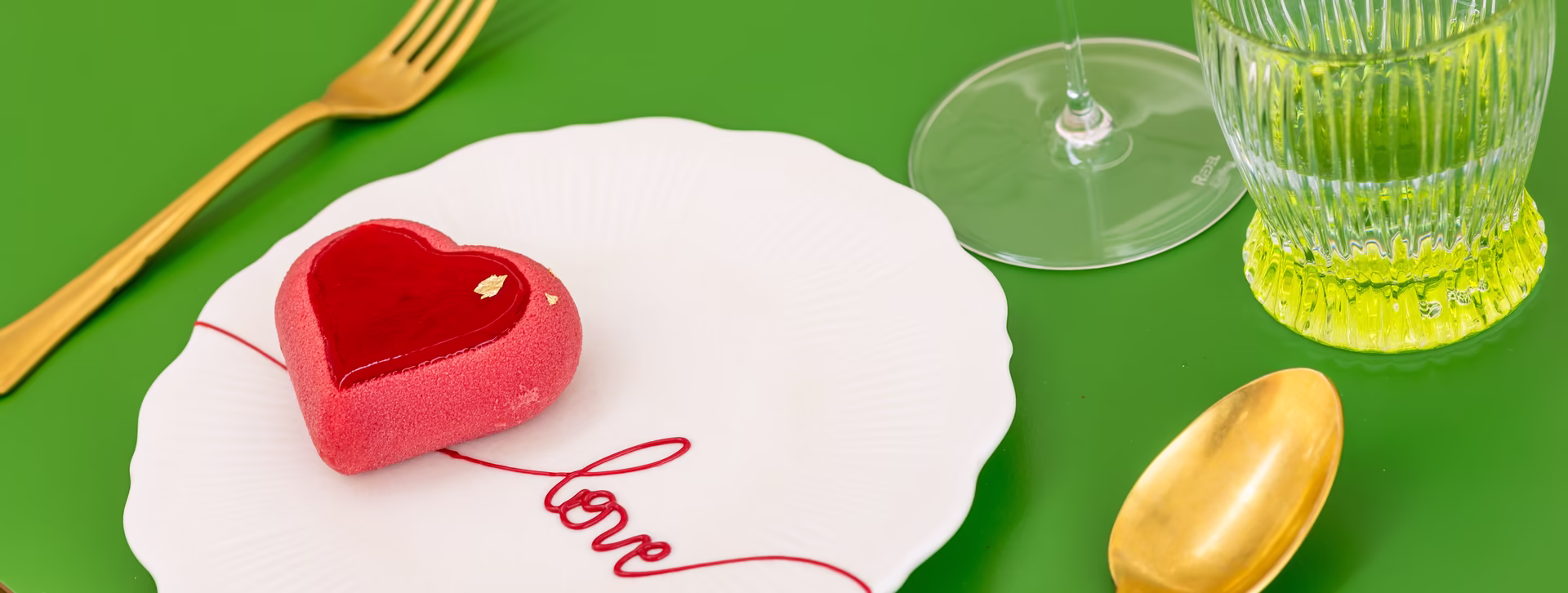 Kleines herzförmiges Küchlein mit goldenem Besteck auf grünem Tisch