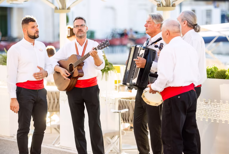 Fünf Männer singen und musizieren draußen beim Abendessen am Meer