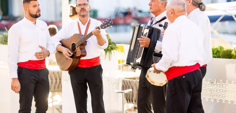 Fünf Männer singen und musizieren draußen beim Abendessen am Meer