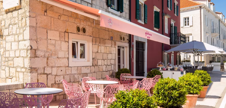 kleine Gelateria von draußen mit Rosa Stühlen bei Sonnenschein