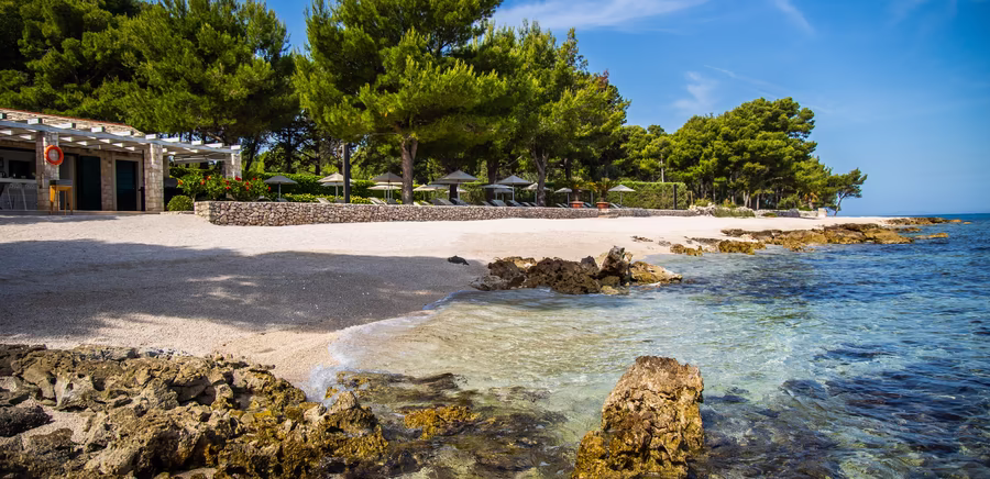 Privater Kieselstrand mit Strandbar, klarem Wasser und vielen Bäumen