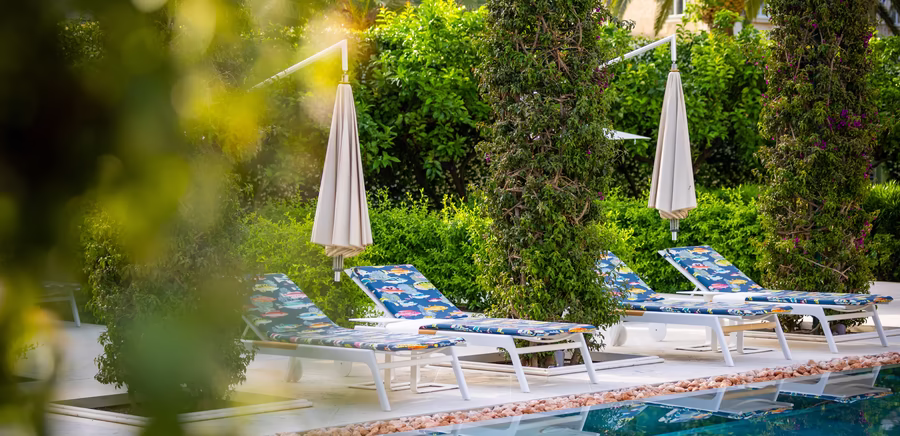 Sonnenliegen mit Schirm vor dem Pool 