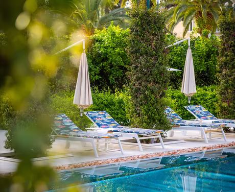 Sonnenliegen mit Schirm vor dem Pool 