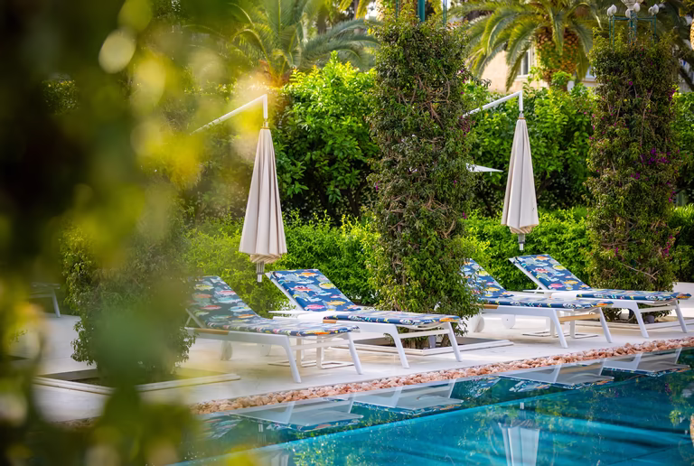 Sonnenliegen mit Schirm vor dem Pool 