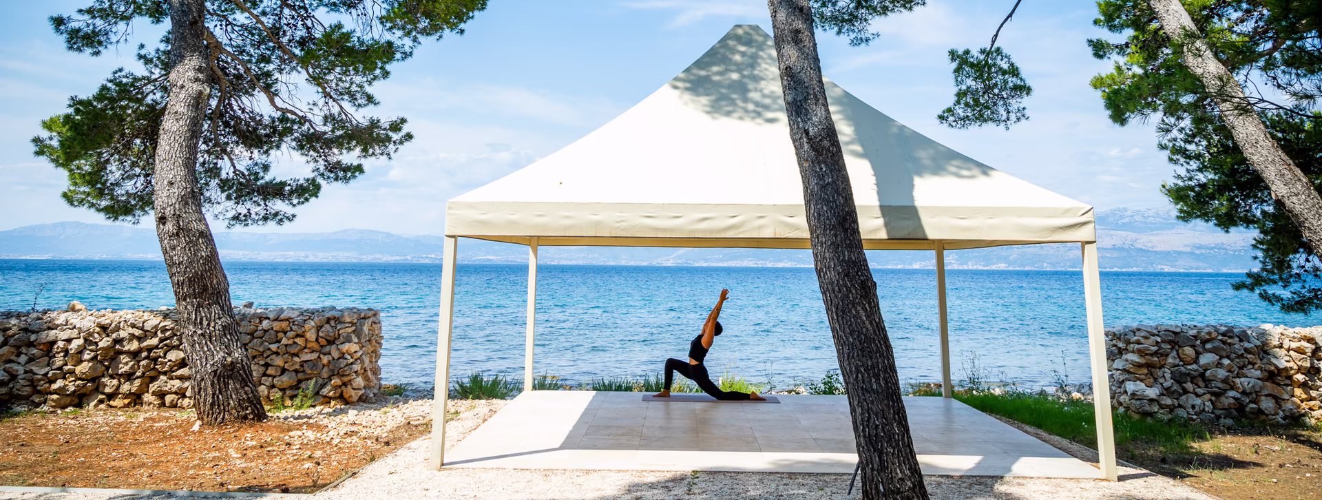Yogalehrerin macht Yogafigur unter einem Sonnenzelt direkt am Meer