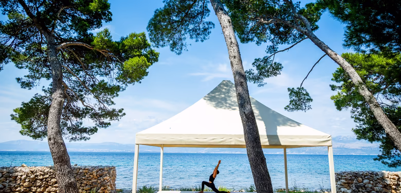 Yogalehrerin macht Yogafigur unter einem Sonnenzelt direkt am Meer