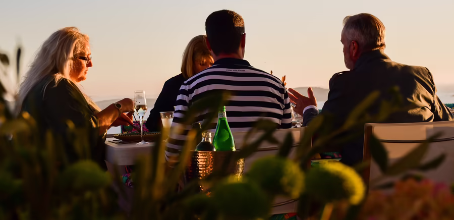 Ein Tisch Erwachsener Menschen isst bei Sonnenuntergang auf einer Dachterrasse