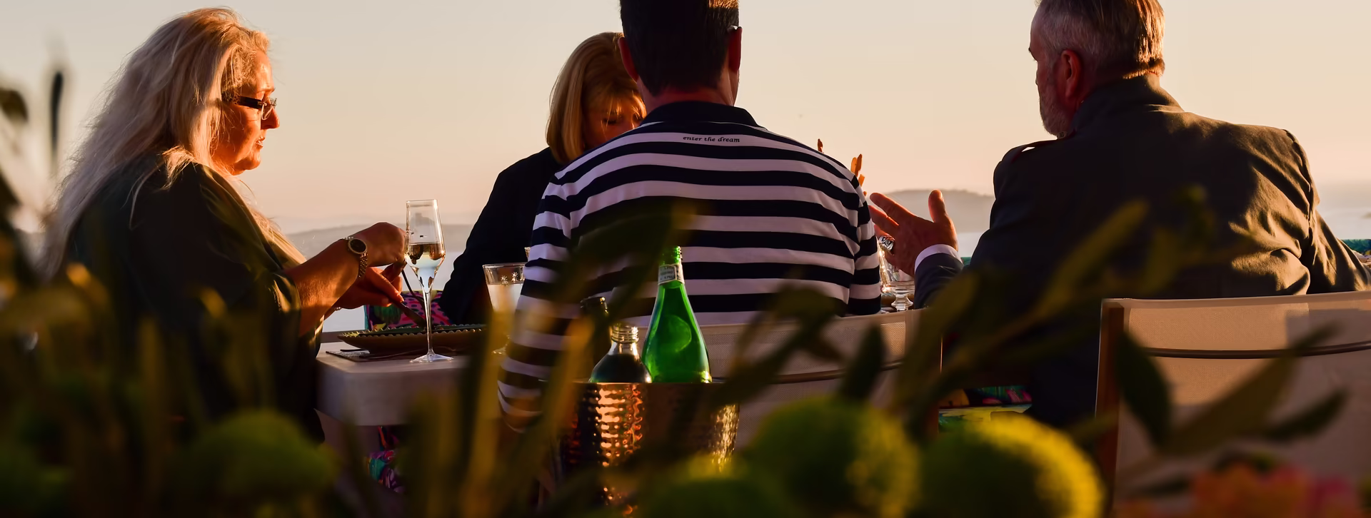 Ein Tisch Erwachsener Menschen isst bei Sonnenuntergang auf einer Dachterrasse